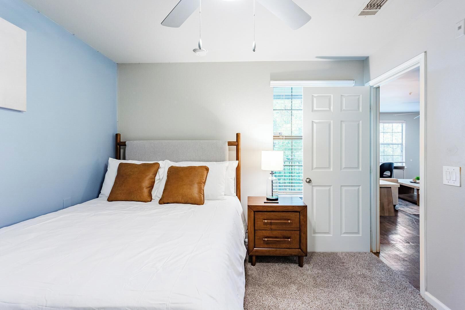 A bedroom with a bed, bedside table, lamp, and a door leading to a bathroom.