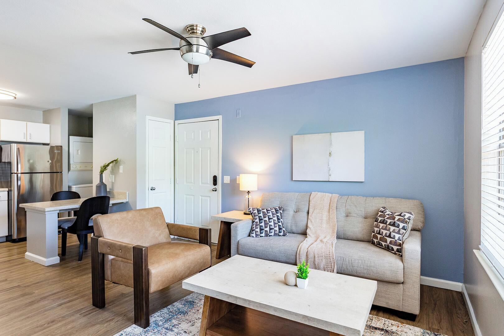 A modern living room with a sofa, armchair, coffee table, and a ceiling fan.