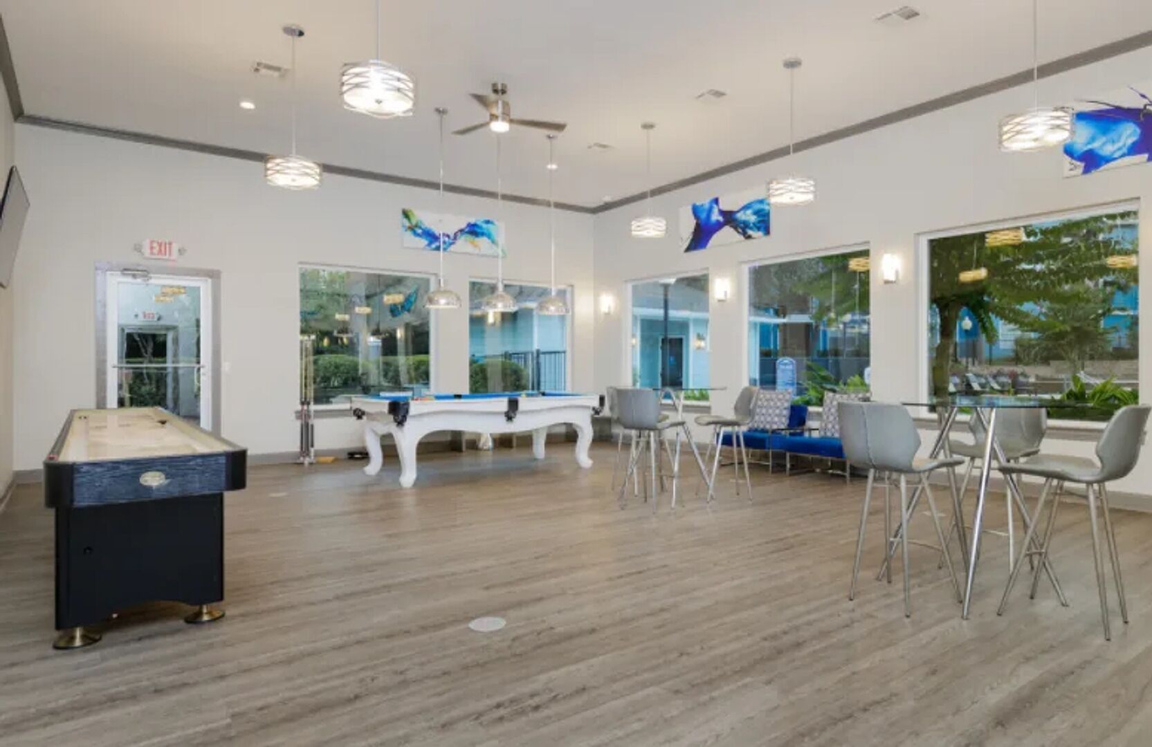 A pool table, seating area, and large windows in a room with a wooden floor.