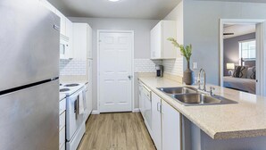 Une cuisine moderne avec des meubles blancs, un réfrigérateur en acier inoxydable, un évier à deux bacs et un plancher en bois.