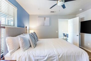 A bedroom with a bed, pillows, a ceiling fan, a TV, and a door leading to a bathroom. - Landing | Incredible 2BD, Clubhouse, Gym (Tallahassee)