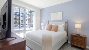 A hotel room with a large bed, a TV, a desk, and a window with a city view. - Landing | Stylish 1BD, Pool, Game Room (New Haven)