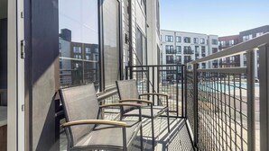 A balcony with chairs, a pool, and modern buildings in the background. - Landing | Stunning 1BD, Game Room, Yoga Studio (New Haven)