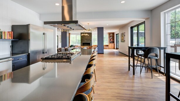 A modern kitchen with a central island, a dining area with chairs, and a view through large windows. - Landing | Stunning 1BD, Game Room, Yoga Studio (New Haven)