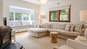 Uma sala de estar moderna com sofá seccional, lareira, um assento junto à janela e uma janela grande com vista para o verde.