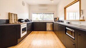 Uma cozinha moderna com armários escuros, piso de madeira, forno embutido, máquina de lavar louça e uma janela grande que proporciona iluminação natural.