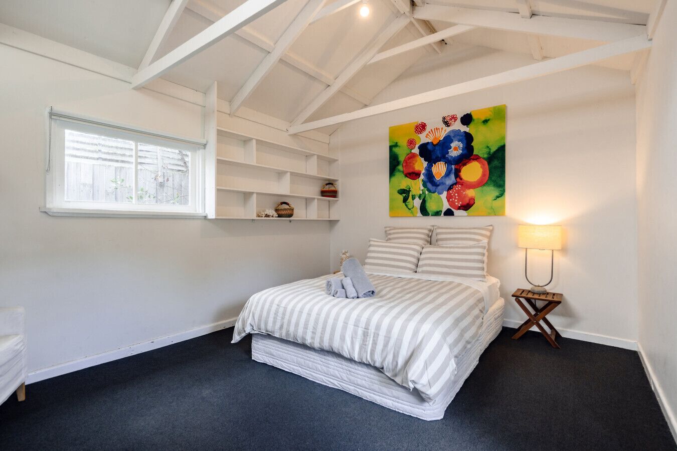 Una camera da letto con un letto, una finestra, un quadro e una lampada da comodino.