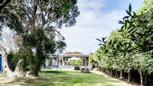 Uma casa com alpendre coberto, trampolim e jardim cercado.