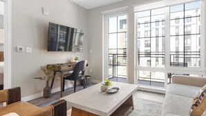 Eine moderne Wohnung mit Essbereich, einem an der Wand befestigten Fernseher und großen Fenstern mit Stadtblick.
