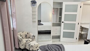 Een slaapkamer met een bed, een stoel, een kledingkast en een spiegel.