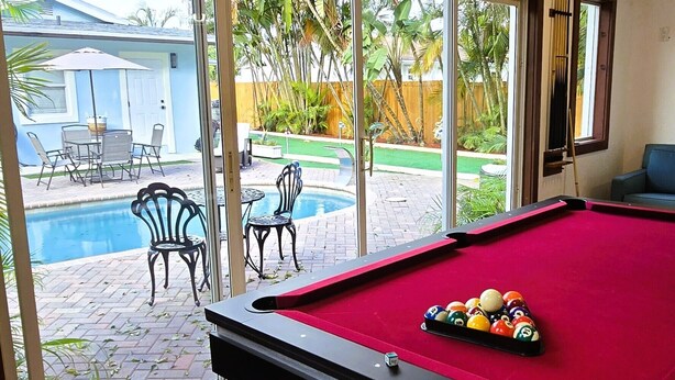 Een pooltafel met ballen, een plafondventilator en uitzicht op een zwembad en terras.