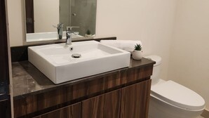 Un bagno moderno con un lavandino bianco, un mobile vanità in legno scuro, uno specchio grande e un water bianco.
