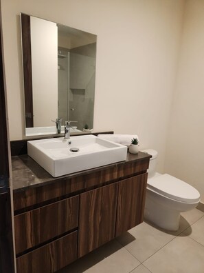 A modern bathroom with a white sink, dark wooden vanity, a large mirror, and a white toilet. - Amazing Apartment! Location + Comfort + Style (pets friendly) (Puerto Vallarta)