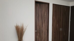 Un corridoio con due porte in legno, un vaso bianco con fiori secchi e un pavimento piastrellato.