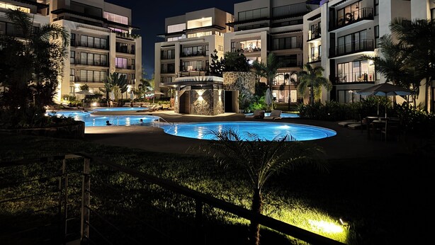 Una vista notturna di un hotel con piscina, numerosi balconi e una vegetazione rigogliosa.