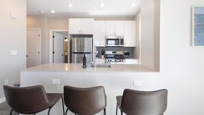 A modern kitchen with a central island, stainless steel appliances, and a view into the adjacent living area.