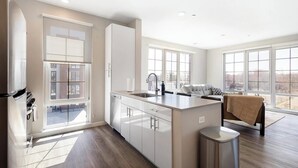 A modern kitchen with a large island, a dishwasher, and a sink. There are large windows providing natural light and views of the outside. - Landing | Spectacular 2BD, Pool, Gym (New Haven)