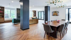 A spacious living area with a large wooden dining table, a green sofa, and a modern chandelier. - Landing | Spectacular 2BD, Pool, Gym (New Haven)