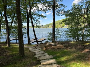 Un chemin de pierres qui mène à un quai au bord d’un lac, entouré d’arbres et de zones herbeuses.