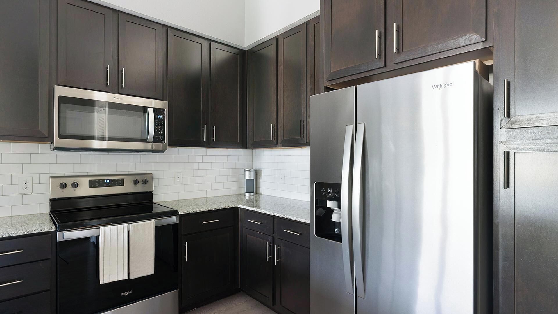 A modern kitchen with dark cabinetry, stainless steel appliances, and white subway tiles.
