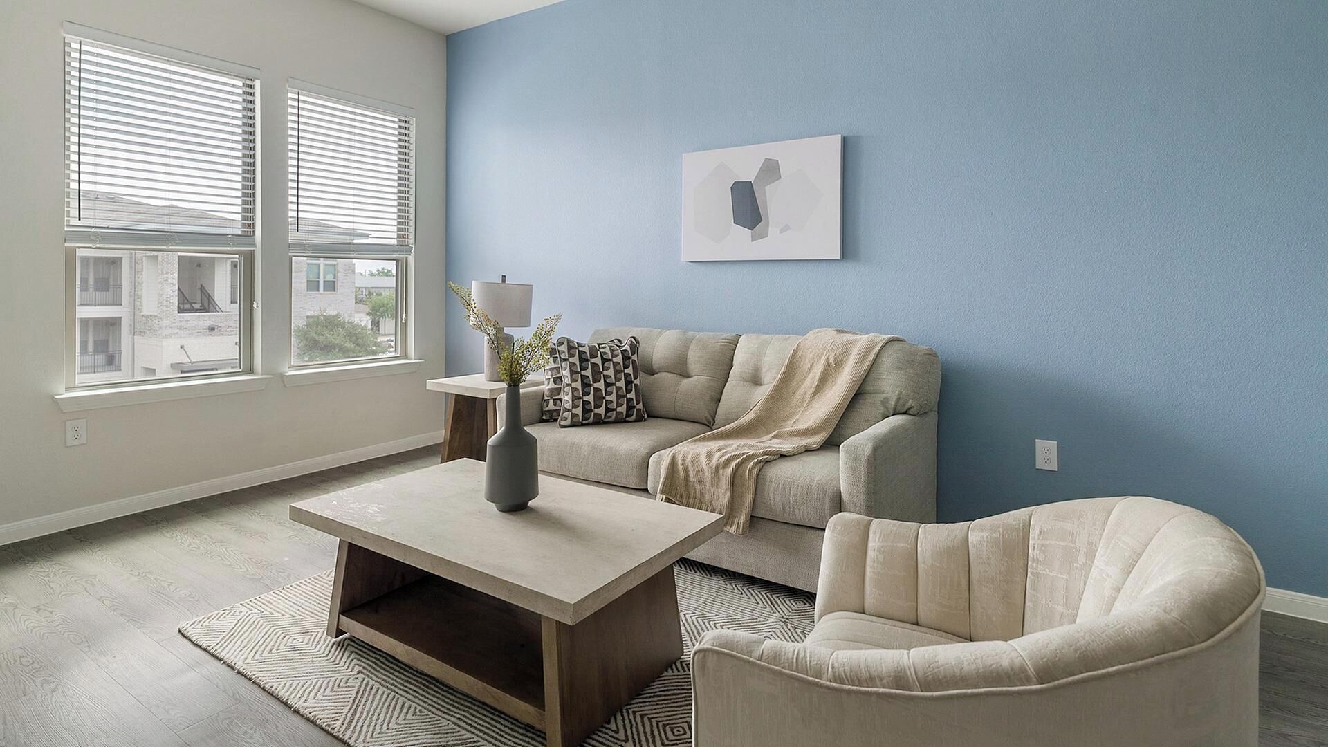 A living room with a sofa, armchair, coffee table, and a painting on the wall.