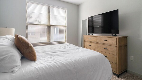 A bedroom with a bed, a dresser, a TV, and a window with blinds.