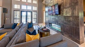 A spacious lobby with a large seating area, a flat-screen TV mounted on a textured wall, and large windows allowing natural light. - Landing | Beautiful 1BD, Gym (New Caney)