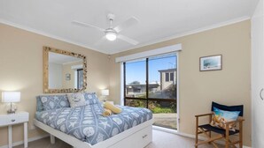 Ein Schlafzimmer mit Bett, Sessel, Deckenventilator, großem Fenster und Blick ins Freie.