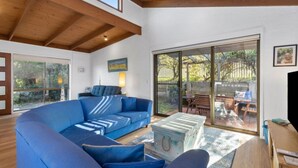 Ein modernes Wohnzimmer mit einem blauen Ecksofa, einem Holztisch und einer Glasschiebetür, die auf eine Terrasss führt.