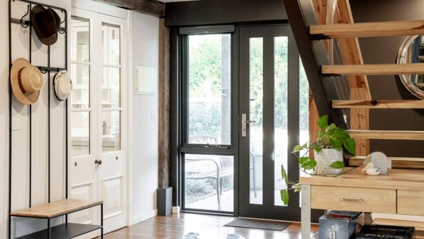 Un interior moderno con una escalera de madera, una puerta blanca con paneles de vidrio y vistas al exterior.