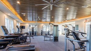 Un gimnasio con cintas de correr, máquinas de pesas y ventiladores de techo.