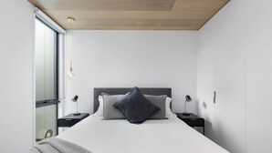Une chambre moderne avec un grand lit, deux tables de chevet avec des lampes, une fenêtre donnant sur un beau paysage et un plafond en bois.