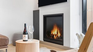 Un salon moderne avec une cheminée, un canapé, une table ronde en bois et une bouteille de vin.