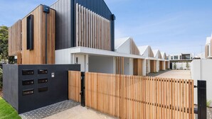 Un bâtiment moderne à la façade noire et blanche, doté d’une clôture en bois et d’une entrée fermée par un portail.