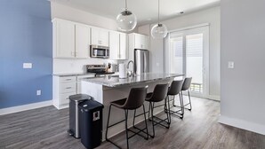 Een moderne keuken met witte kasten, een centraal eiland met barkrukken, roestvrijstalen apparatuur en hanglampen.