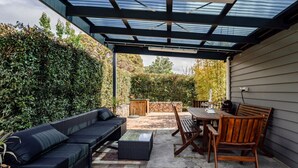 Une terrasse extérieure dotée d’un espace salon abrité, d’une table avec des chaises et d’un mur en pierre.