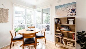 Un coin repas avec une table ronde, quatre chaises, un ventilateur de plafond, une bibliothèque remplie de livres et un tableau accroché au mur.