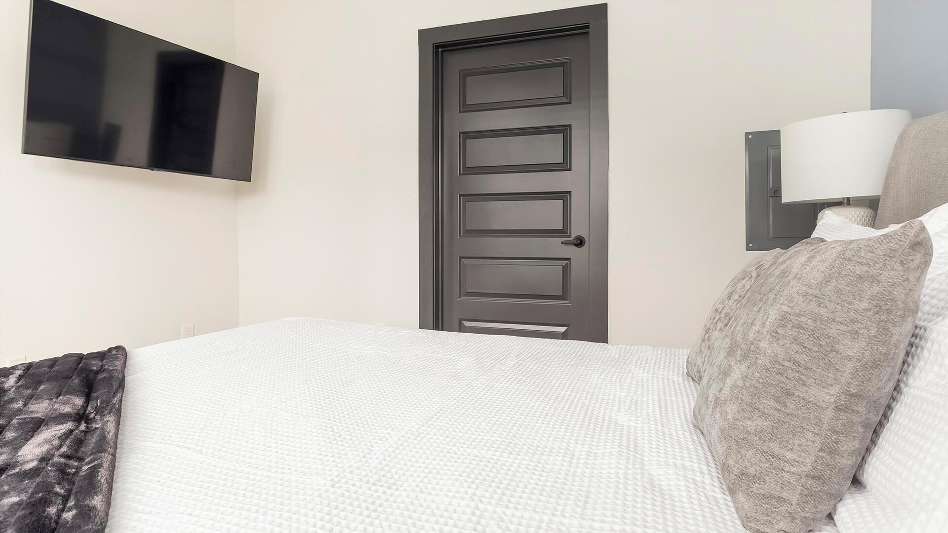Une chambre d’hôtel avec un lit, une porte, un téléviseur fixé au mur et une lampe.