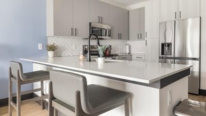 Uma cozinha moderna com ilha central, eletrodomésticos de aço inoxidável e armários cinzas.