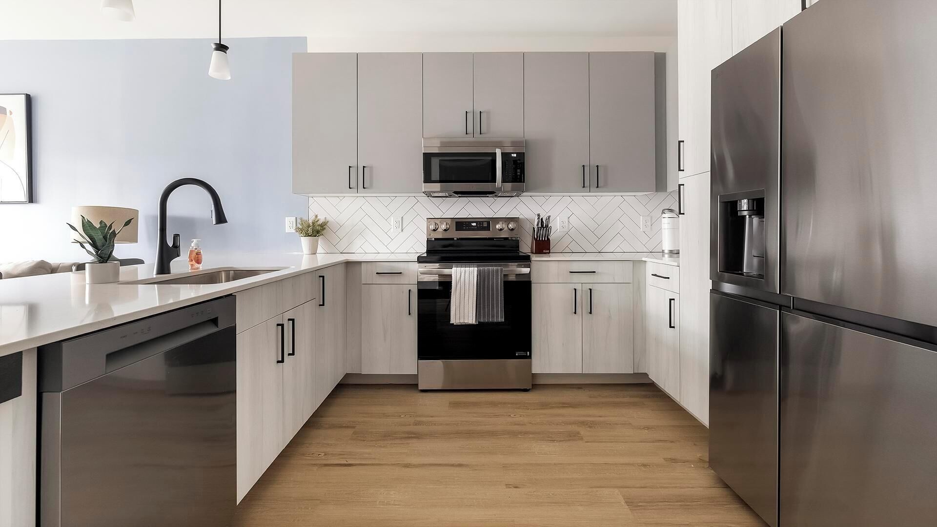 Et moderne køkken med rustfrie hårde hvidevarer, lyse træskabe og et backsplash med fiskebensmønster.
