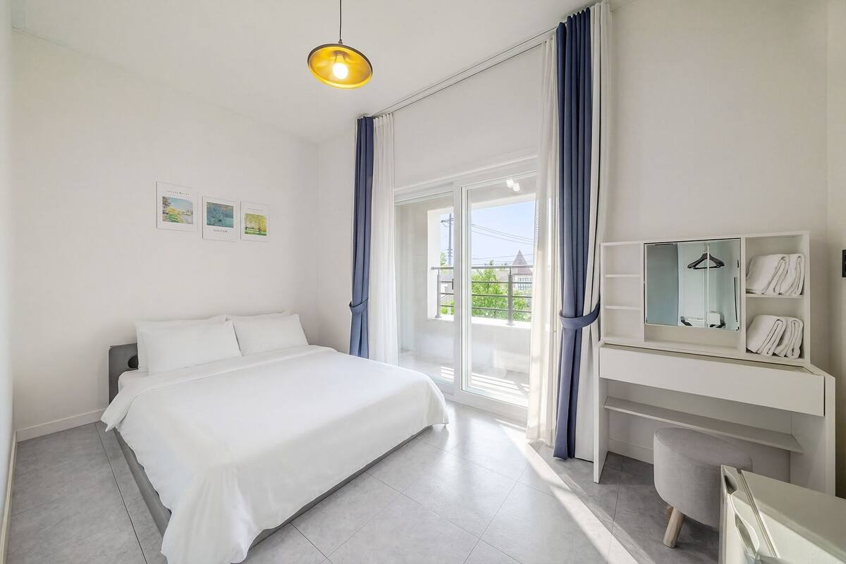 Habitación de hotel con cama, escritorio con espejo y vistas a través de un ventanal.