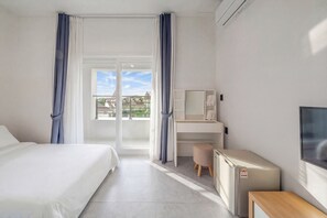 Une chambre d’hôtel comprenant un lit, un bureau, un petit réfrigérateur, une télévision et un balcon avec des rideaux.