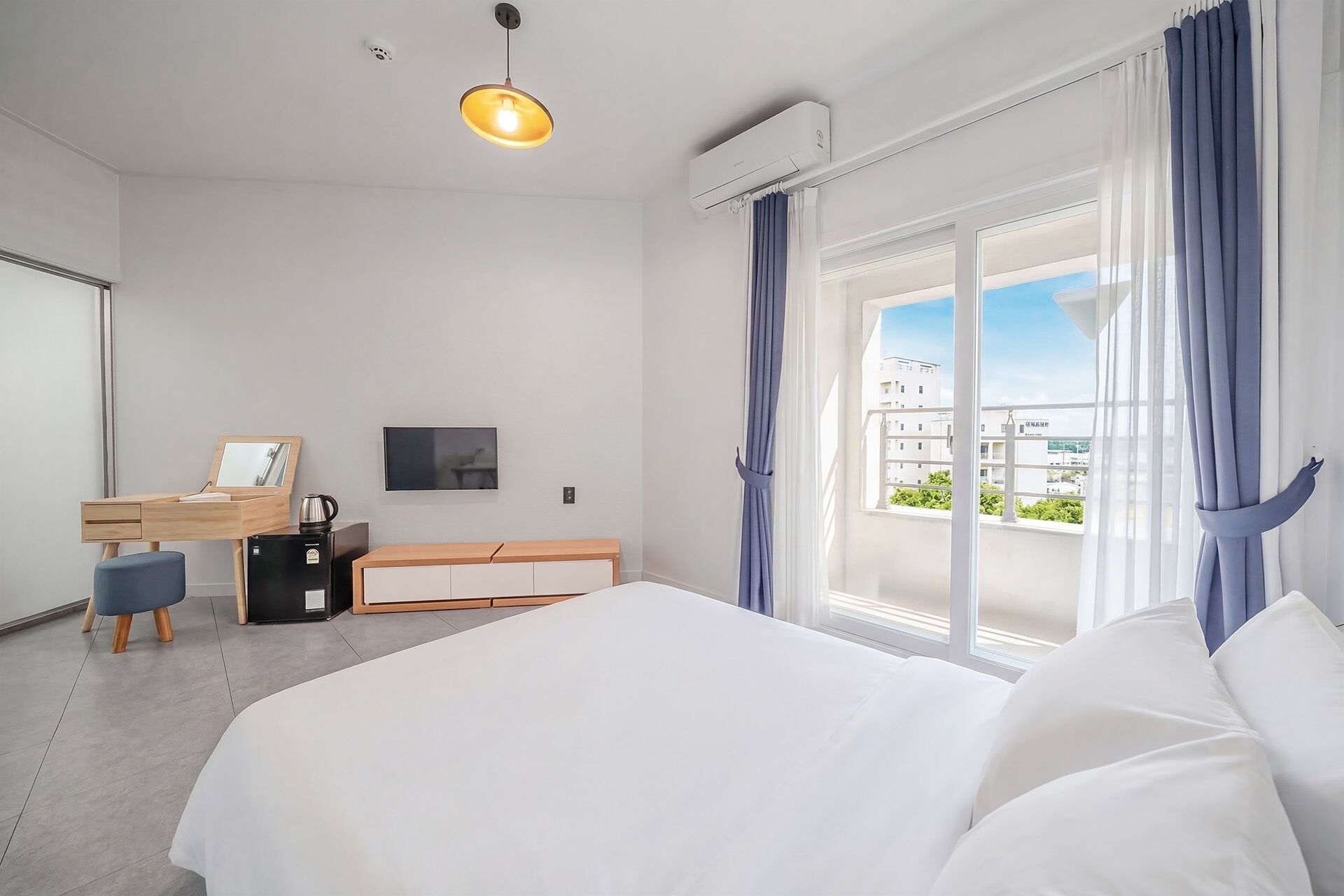 A modern hotel room with a bed, a desk with a chair, a television, and a window with curtains.