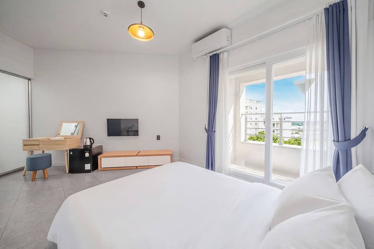 Una habitación de hotel moderna con una cama, un escritorio con una silla, un televisor y una ventana con cortinas.