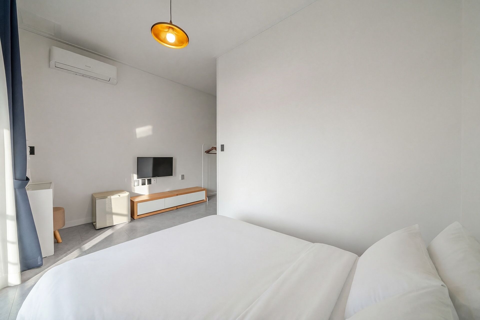 Une chambre moderne avec un lit, une télévision, un bureau et un luminaire suspendu.