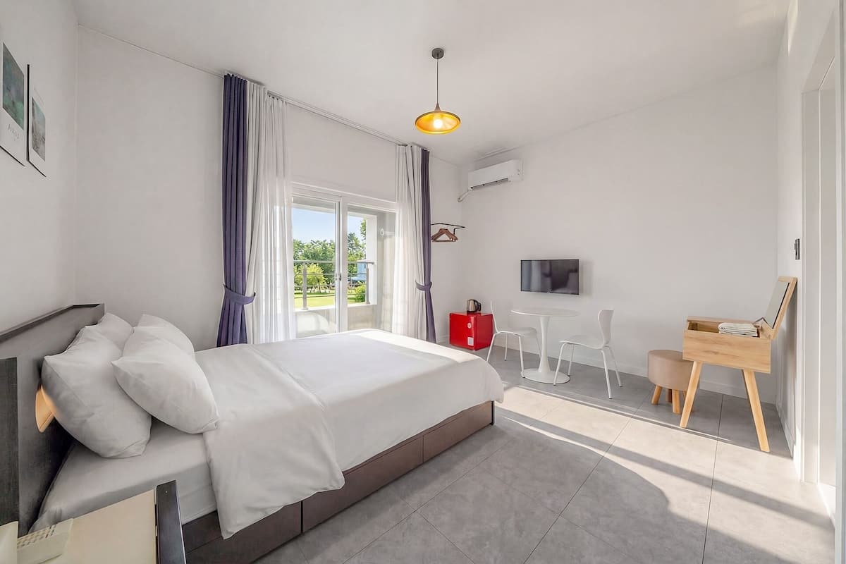Un dormitorio moderno con cama, televisor, escritorio y vistas al verdor exterior.