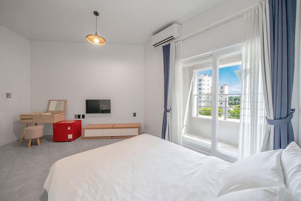 Un dormitorio con cama, un escritorio con silla, televisión y ventana con cortinas.