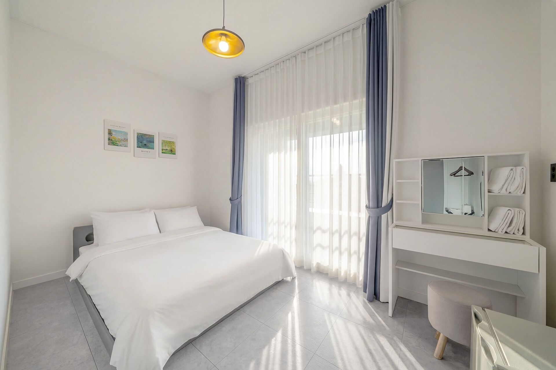 A hotel room with a bed, a desk with a mirror, and a hanging towel rack.