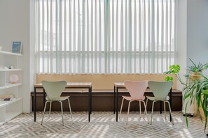 Una habitación con ventana, dos sillas, una mesa, una estantería y una planta en maceta.