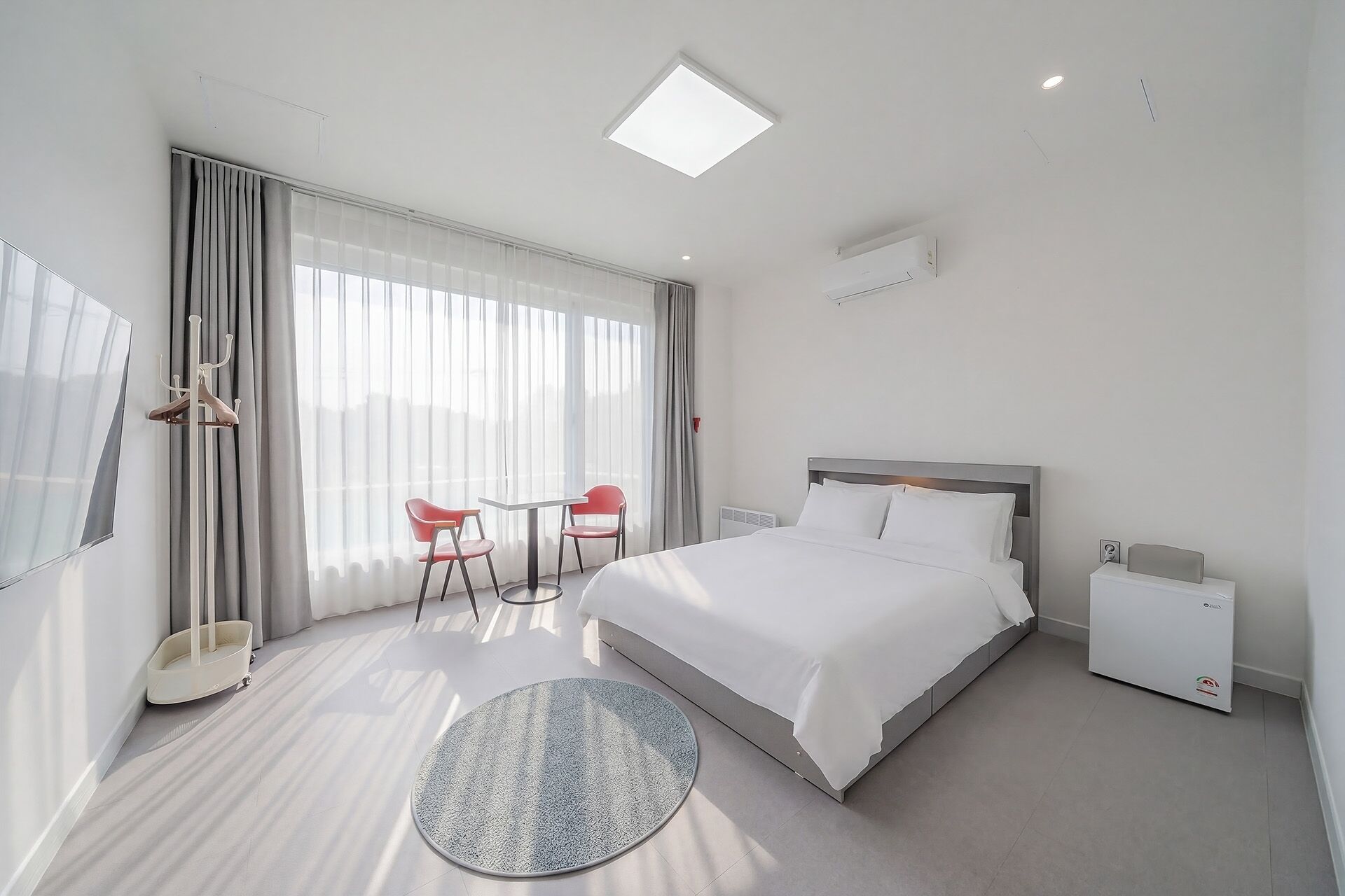 A hotel room with a bed, a round rug, a table with chairs, a TV, and a window with curtains.